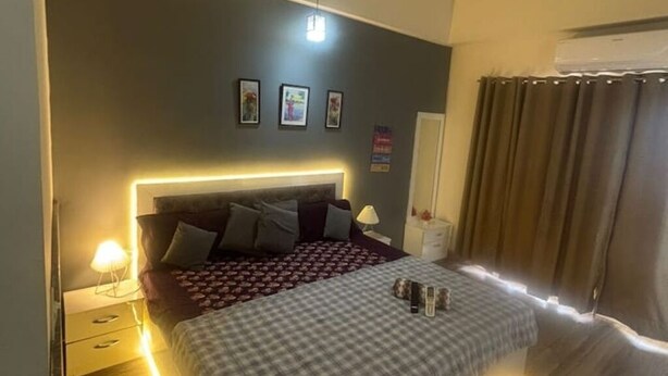 Une chambre à coucher avec un grand lit, des tables de chevet, une lampe fixée au mur et une fenêtre avec des rideaux.