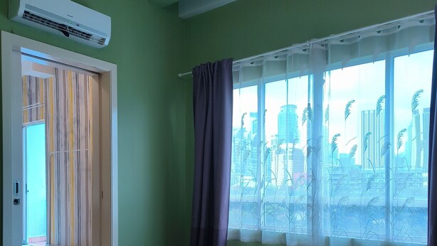 Quarto de hotel com cama, janela com cortinas e porta com cortinas listradas, além de um aparelho de ar condicionado.