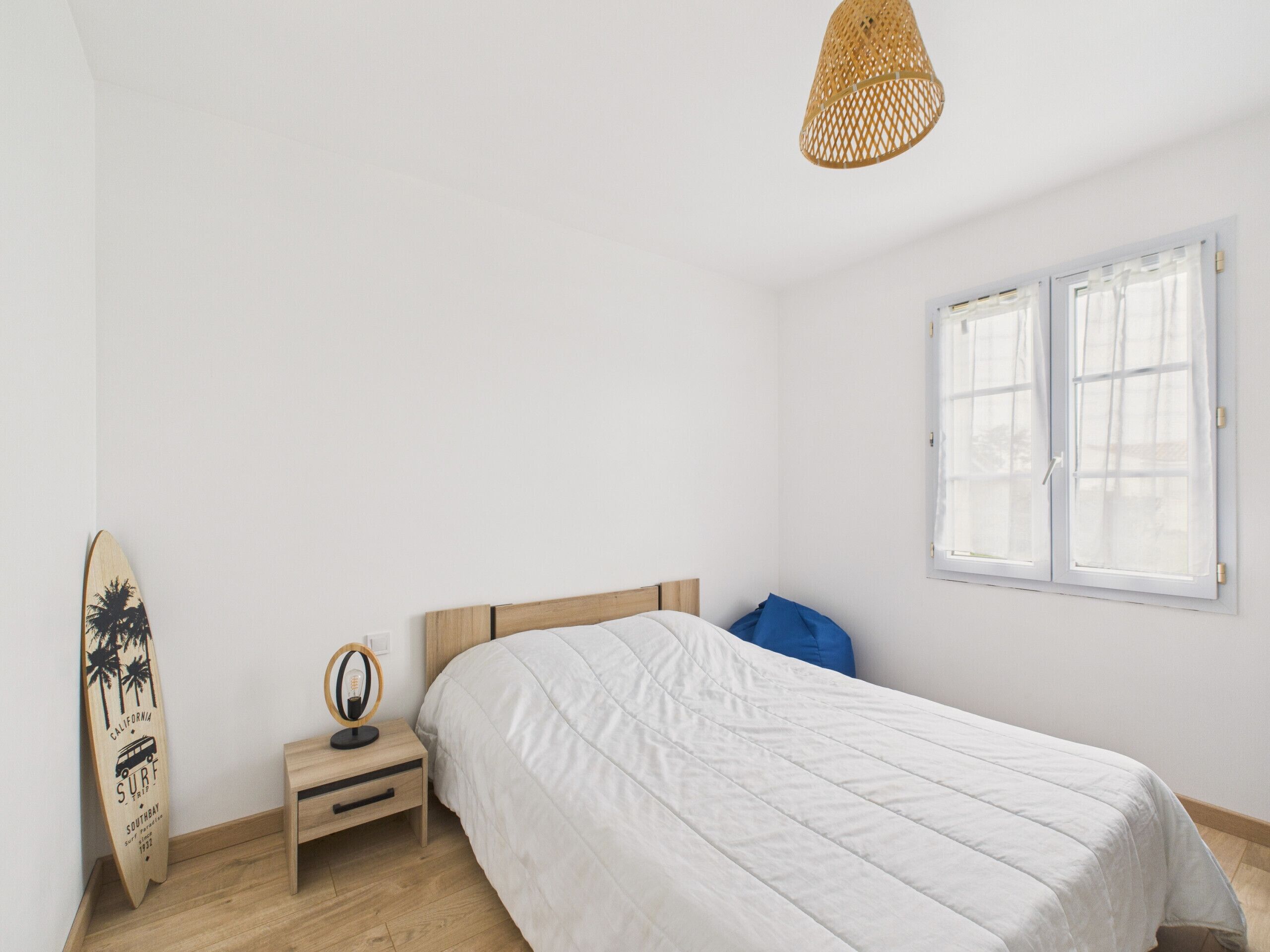 Een slaapkamer met een bed, nachtkastje, een surfplank en een raam.
