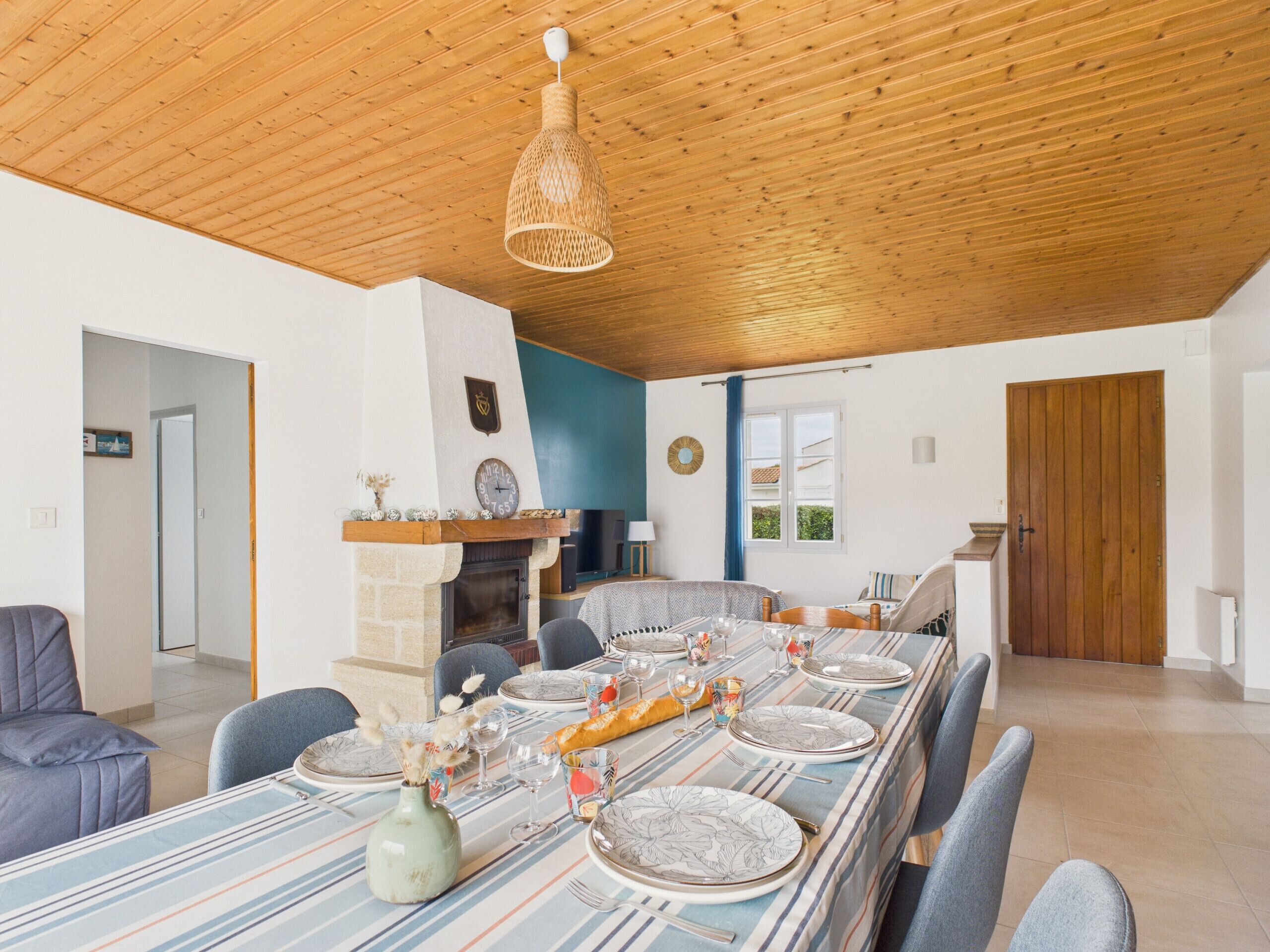 A dining room with a long table set for six, a fireplace, and a wooden ceiling.