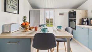 Een keuken met een houten tafel, blauwe stoelen, een koelkast, een magnetron en een koffiezetapparaat.