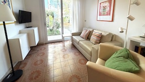 Een woonkamer met een bank, een televisie, een tafel en een deur naar een balkon.