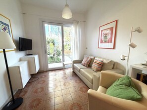 Ein Wohnzimmer mit einer Couch, einem Fernseher, einem Tisch und einer Tür, die auf einen Balkon führt.