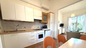 Een moderne keuken met witte kasten, een fornuis en een spoelbak. Er is een zithoek met oranje stoelen en een tafel.