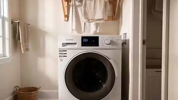 A front-loading washing machine with a digital display, a basket, and a towel rack in a laundry room.