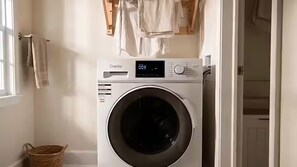 Une machine à laver à chargement frontal dotée d’un écran numérique, d’un panier et d’un porte-serviettes, dans une buanderie.