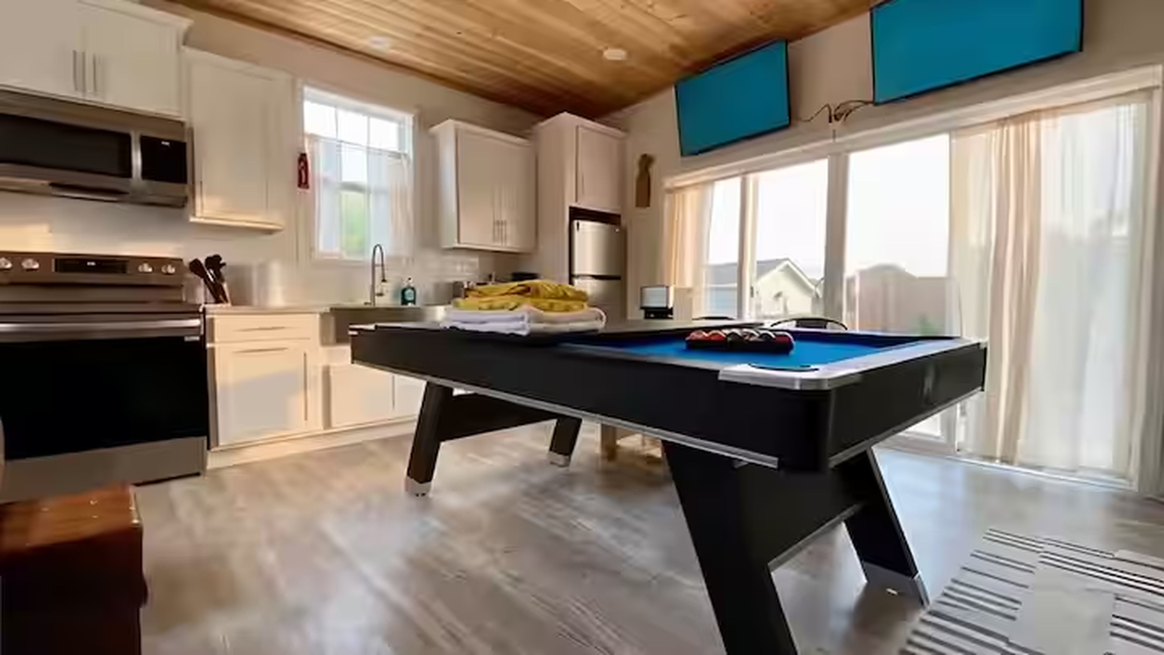 Une cuisine moderne dotée d’un billard, d’appareils électroménagers en acier inoxydable et de grandes fenêtres.