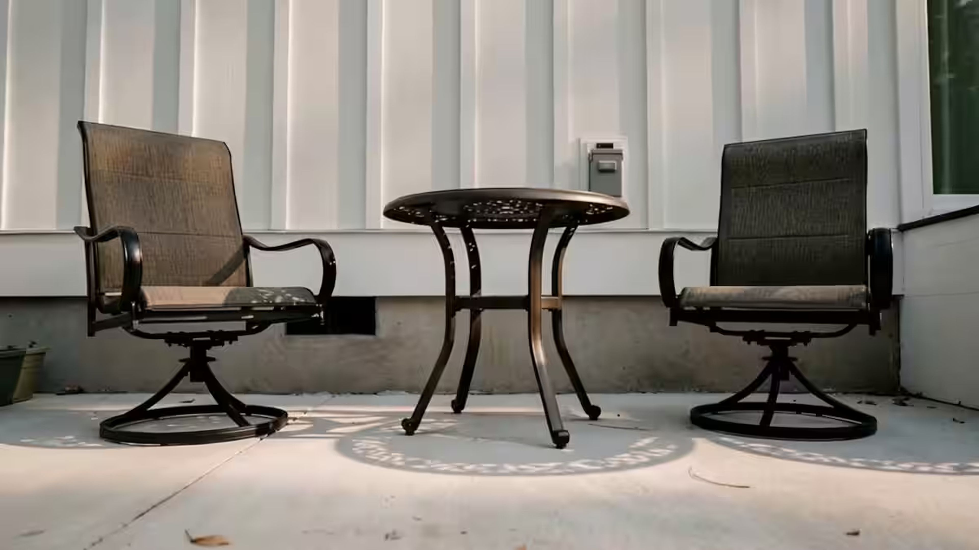 Deux chaises et une table sont placées à l’extérieur, devant un bâtiment dont le revêtement est constitué de panneaux verticaux.