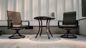 Two chairs and a table outside a building with vertical siding.