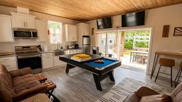 A modern kitchen with white cabinets, a pool table, and a dining area with a bar.