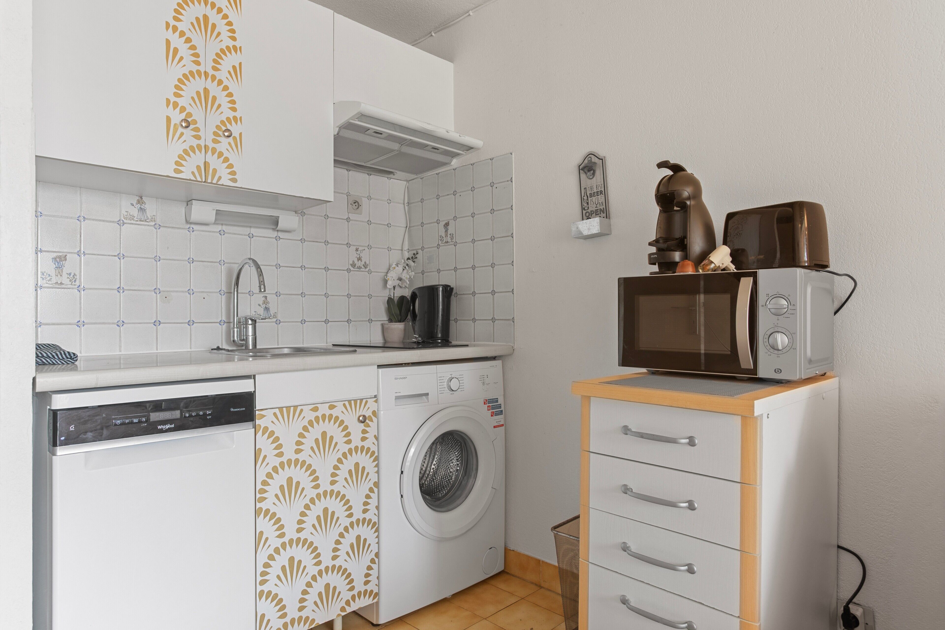 A compact kitchen with a dishwasher, washing machine, microwave, and a small cabinet with drawers.