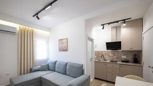 Een moderne woonkamer met een grijze hoekbank, een flatscreen-tv en een keuken met een marmeren aanrechtblad en kastjes.