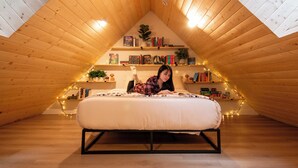 Un dormitorio tipo loft con techo inclinado, una cama, estanterías y luces de adorno.