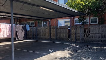 Un espace de stationnement couvert, doté d’un toit en métal, d’une clôture en bois et d’un bâtiment en briques en arrière-plan.