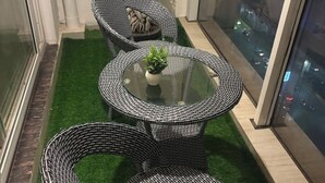 A balcony with wicker furniture, a glass table, and a small potted plant. - Premium 14th-Floor Studio with Balcony & Stunning City Views (Noida)
