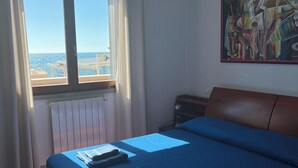 A bedroom with a bed, a radiator, a window with curtains, a painting on the wall, and a view of the sea. - Lo scoglietto apartment 20 mt from the sea (Rosignano Solvay)