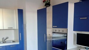 A modern kitchen with blue cabinets, a dining table with a blue tablecloth, and a small plant on the counter. - Lo scoglietto apartment 20 mt from the sea (Rosignano Solvay)