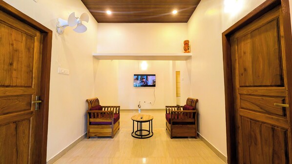 A hallway with wooden doors, a television mounted on the wall, and two wooden chairs with cushions.