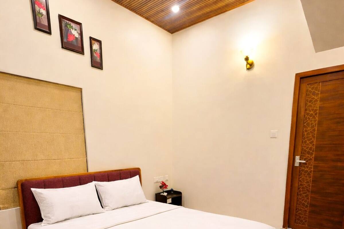 A neatly made bed in a room with a wooden ceiling, a wooden door, and a nightstand with a lamp.
