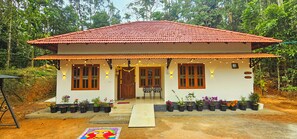 A two-story house with a red-tiled roof, wooden windows, and a porch with string lights.