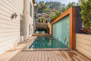 A pool area with wooden decking, a tiled wall, and lounge chairs. - ELIVAAS prive The Royce Lilly Luxe 4 BHK (Kasauli)