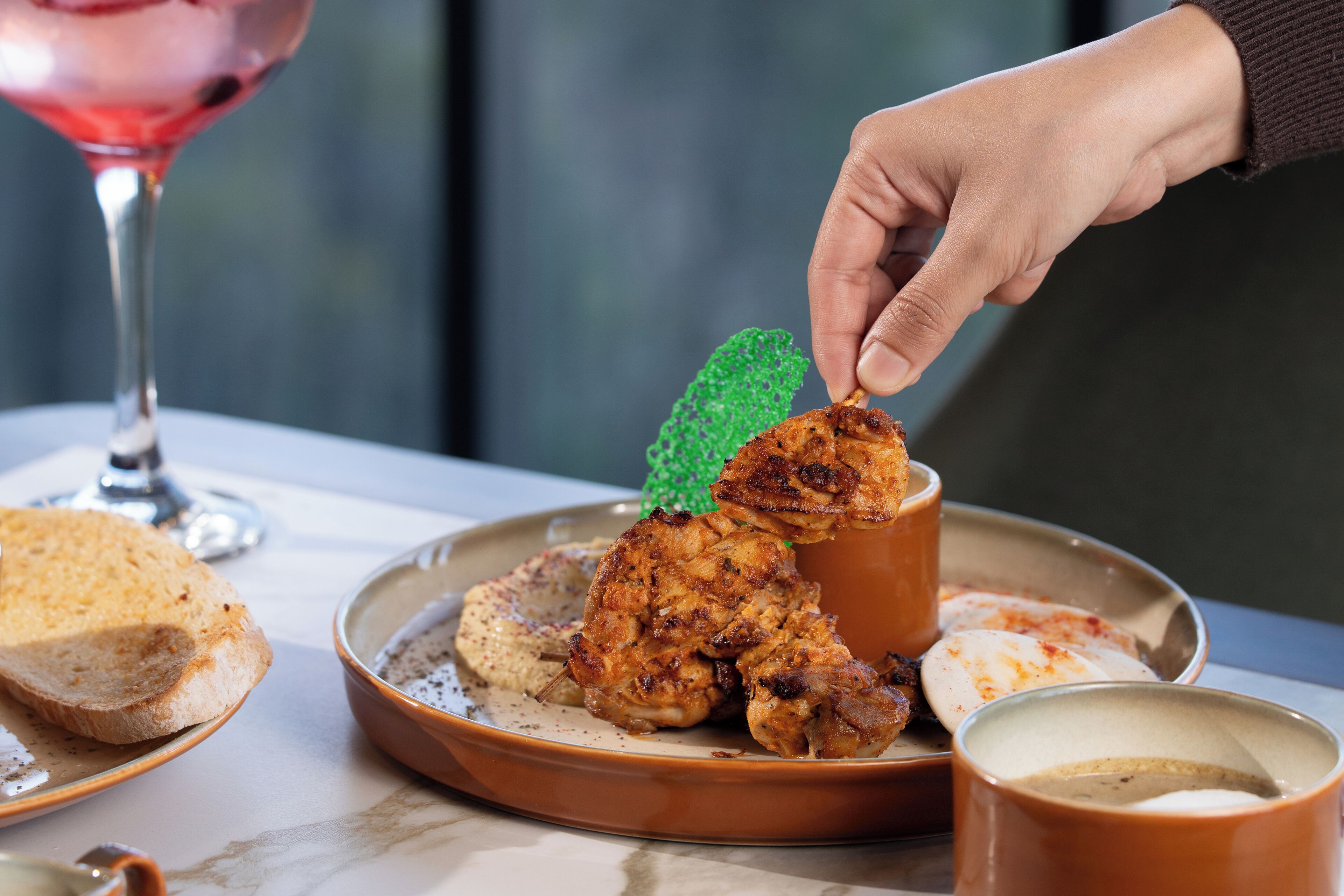 A plate with grilled chicken and bread, a glass of pink drink, and a green garnish on a table.
