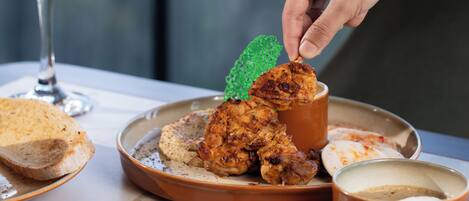 A plate with grilled chicken and bread, a glass of pink drink, and a green garnish on a table.