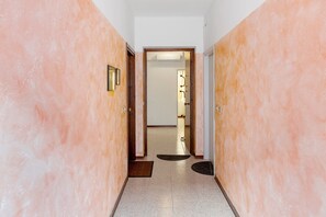Un couloir aux murs roses, une porte au fond et un tapis sur le sol.