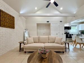 Ein modernes Wohnzimmer mit einem beigen Sofa, einem Couchtisch aus Holz mit einer Pflanze und einer Küche im Hintergrund.