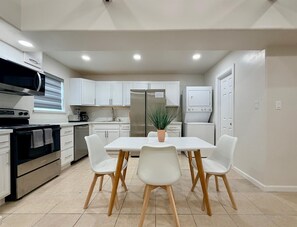 Une cuisine moderne avec des meubles blancs, un réfrigérateur en acier inoxydable, un four à micro-ondes et une cuisinière. On y trouve une table à manger avec quatre chaises et une plante en pot.