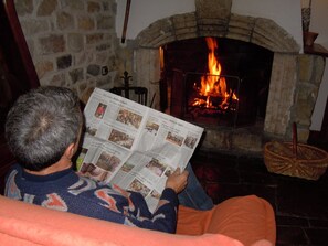 Eine Person sitzt auf einem Sofa vor einem Kamin aus Stein, in dem Feuer brennt.