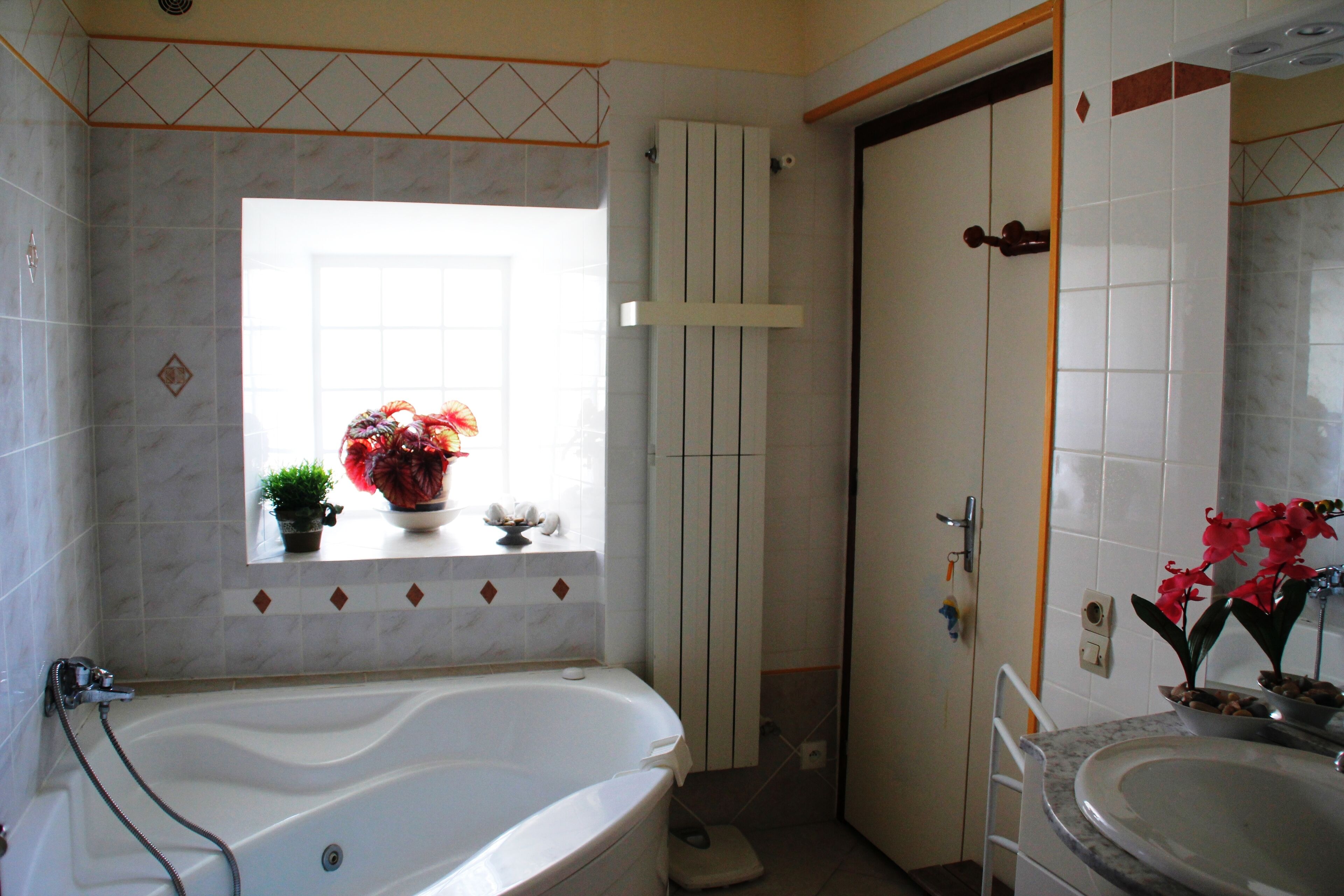 A bathroom with a bathtub, a sink, and a window with a potted plant.