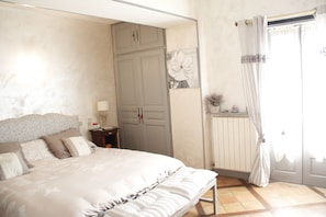 Ein Schlafzimmer mit Bett, Kleiderschrank, Nachttisch, Lampe und einem Fenster mit Vorhängen.