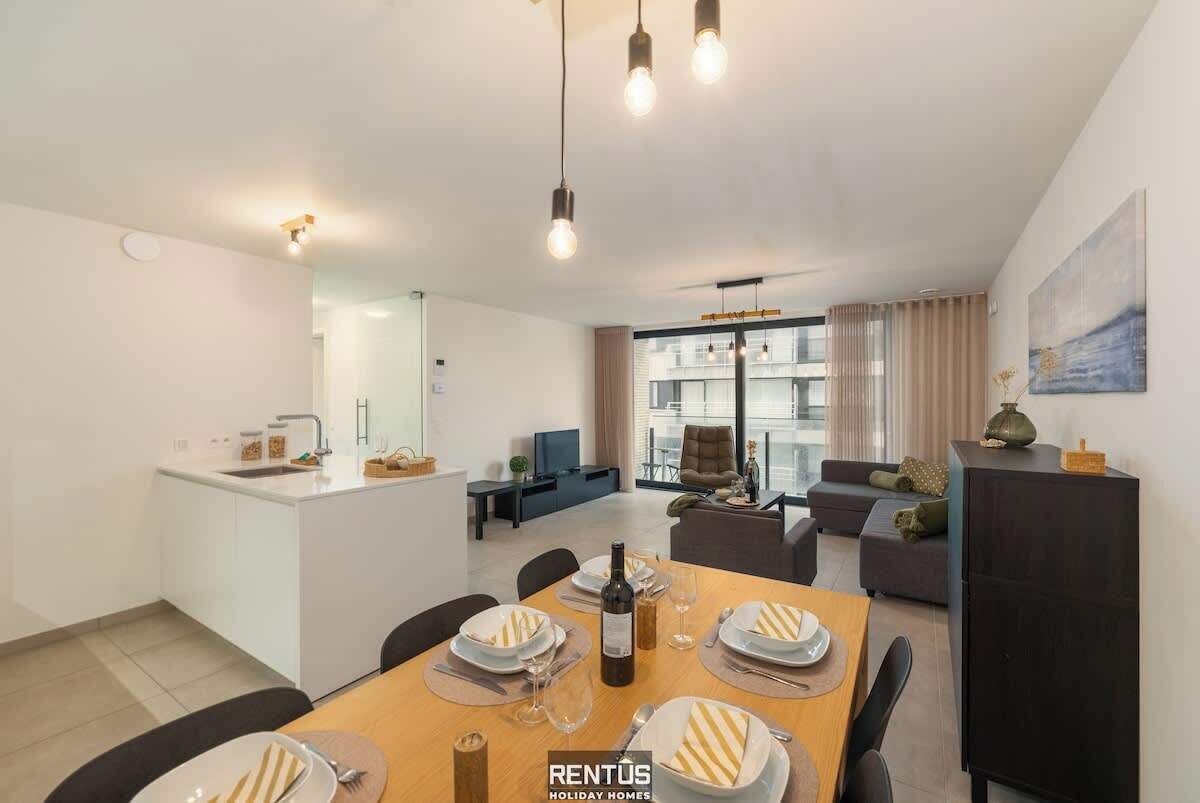 Un appartement moderne comprenant un coin repas, une cuisine, un salon et une grande fenêtre.
