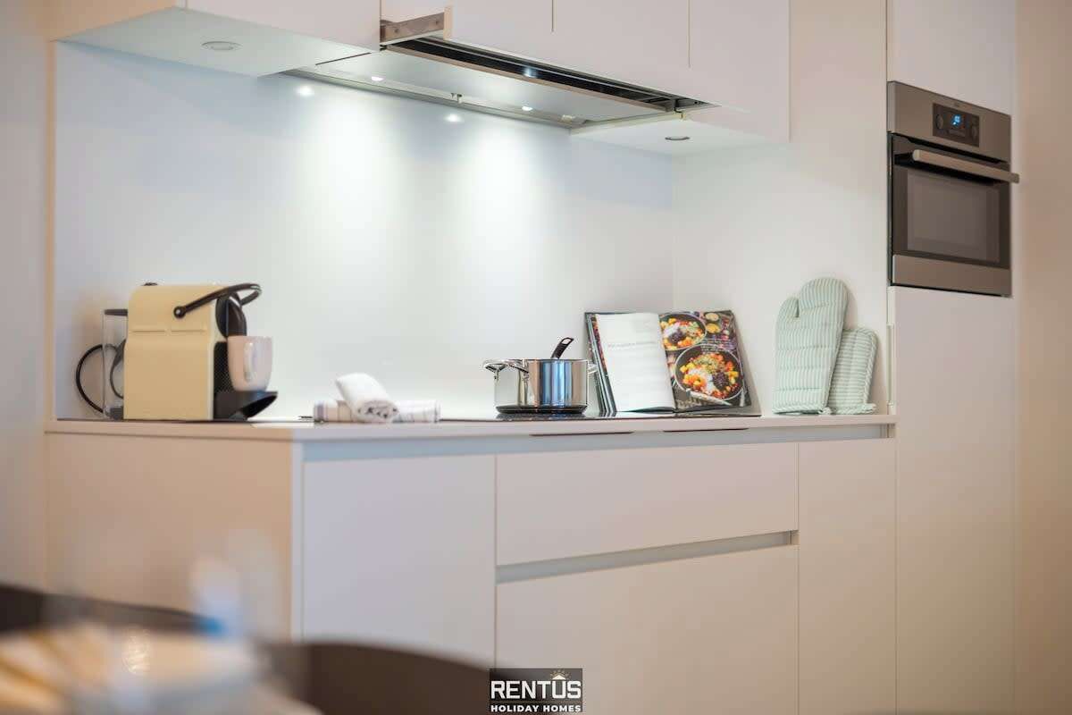 A modern kitchen with a built-in oven, a coffee machine, and a small refrigerator.