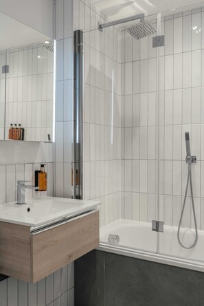 Une salle de bain moderne avec une douche à parois de verre, un meuble-lavabo blanc doté d’un tiroir en bois et un grand miroir.