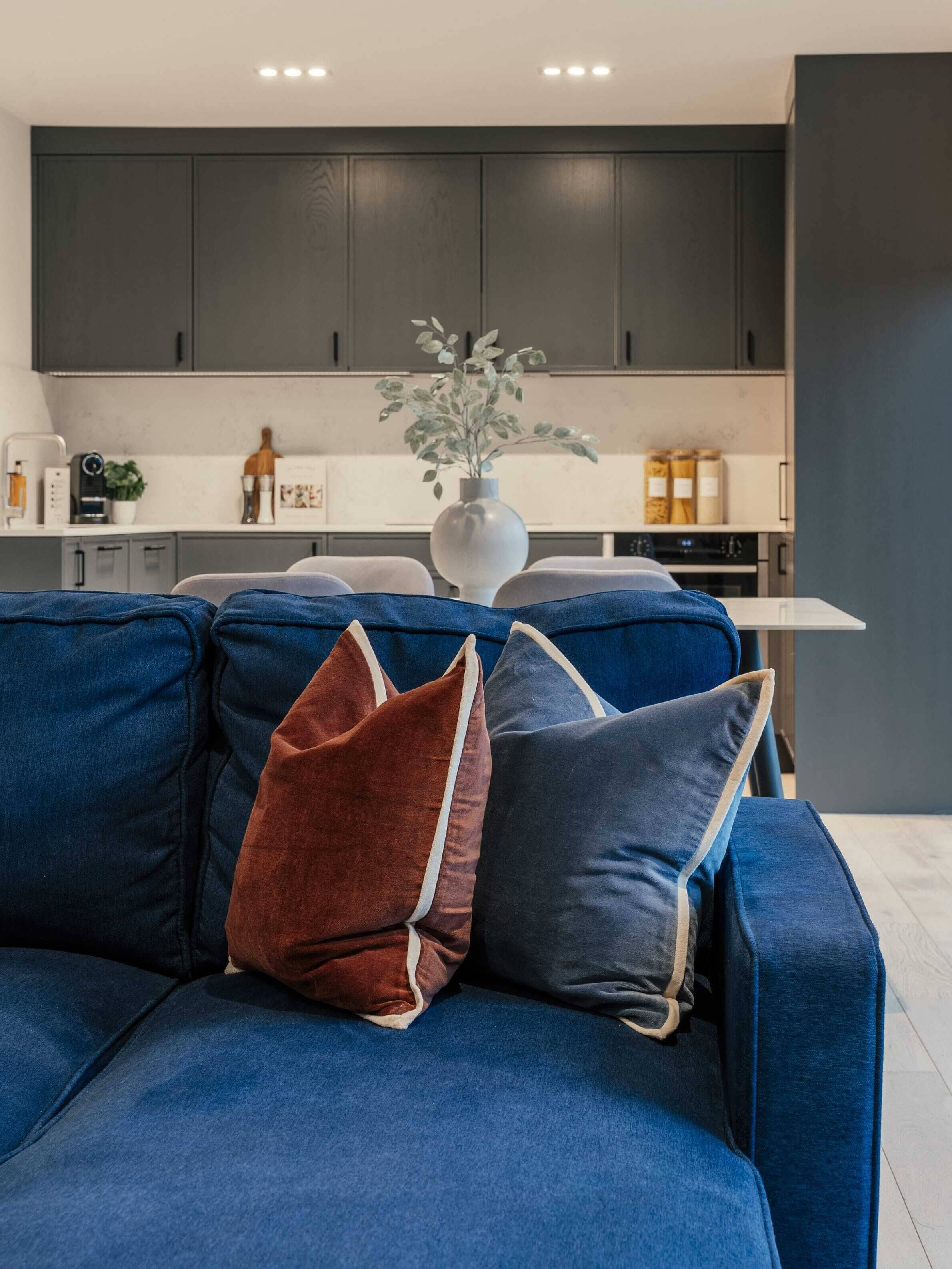 Ein modernes Wohnzimmer mit einem dunkelblauen Sofa, zwei Kissen und einer weißen Vase mit Pflanze.