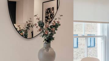 A modern room with a white table and chairs, a large mirror, and a vase with flowers.