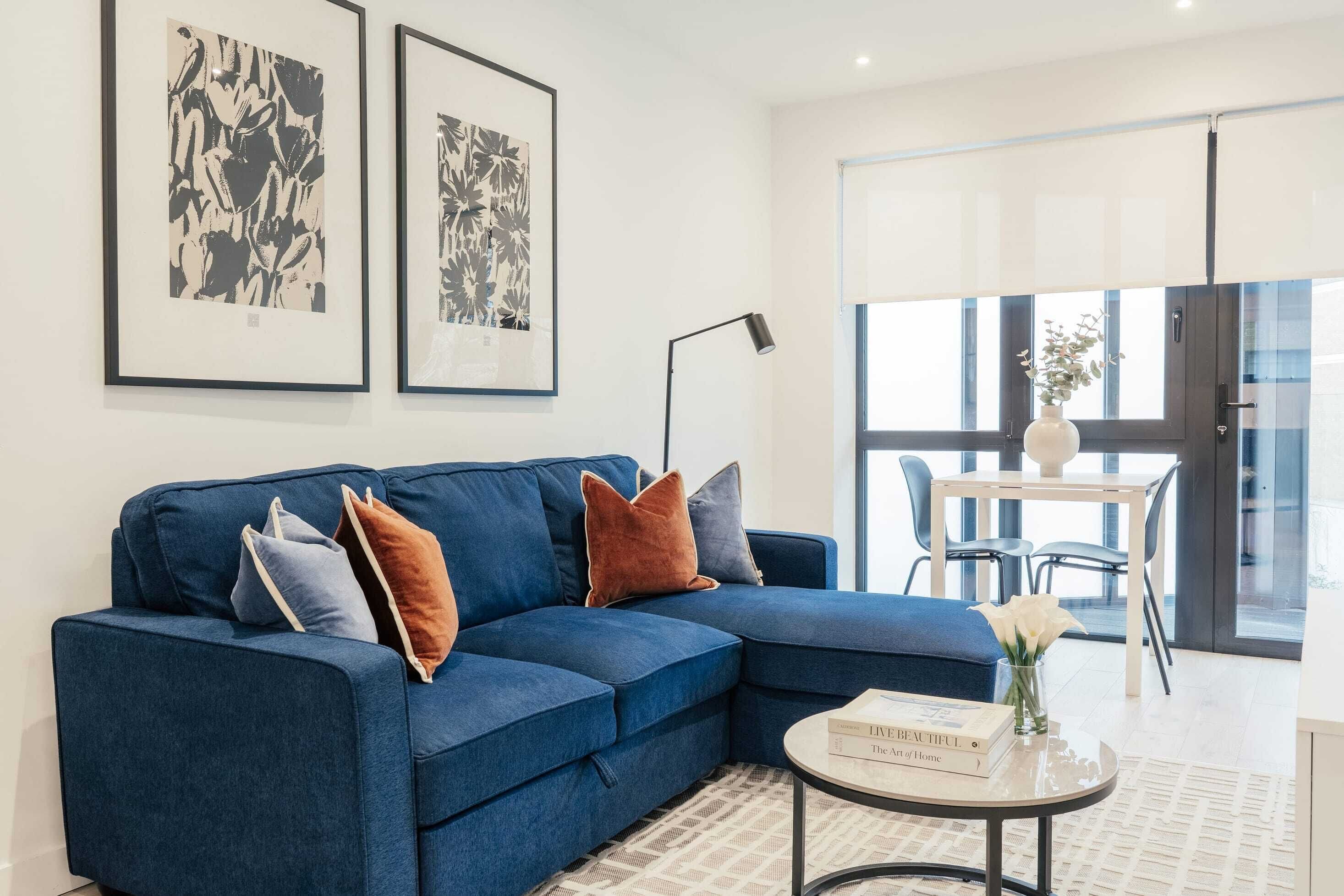 A modern living room with a blue sectional sofa, a round coffee table, and two framed abstract artworks on the wall.
