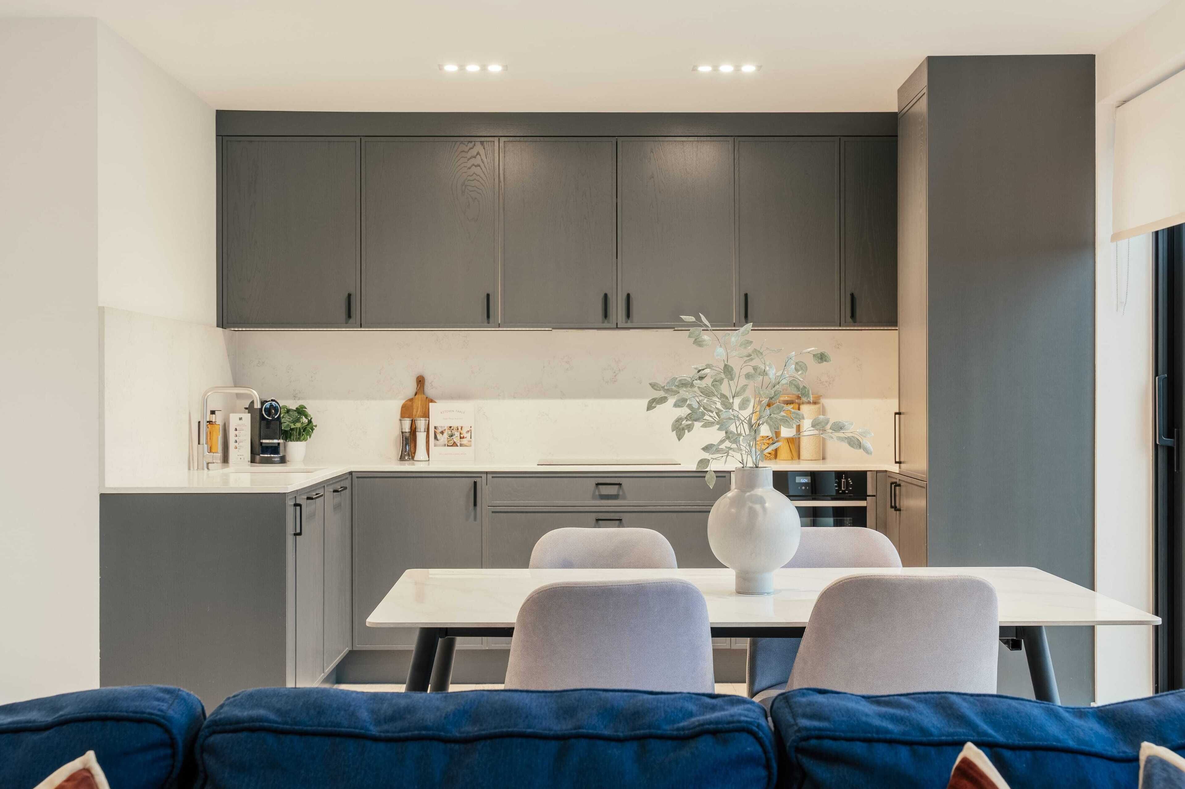 A modern kitchen with grey cabinets, a white countertop, and a dining area with a white table and grey chairs.