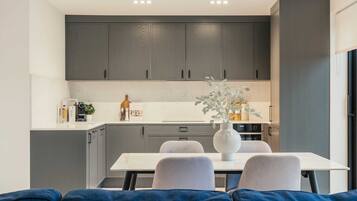 A modern kitchen with grey cabinets, a white countertop, and a dining area with a white table and grey chairs.