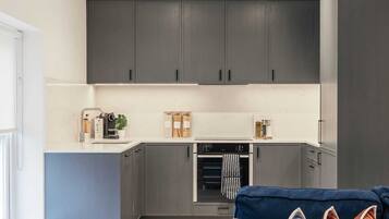 A modern kitchen with grey cabinets, a built-in oven, and a countertop with a coffee machine and a plant.