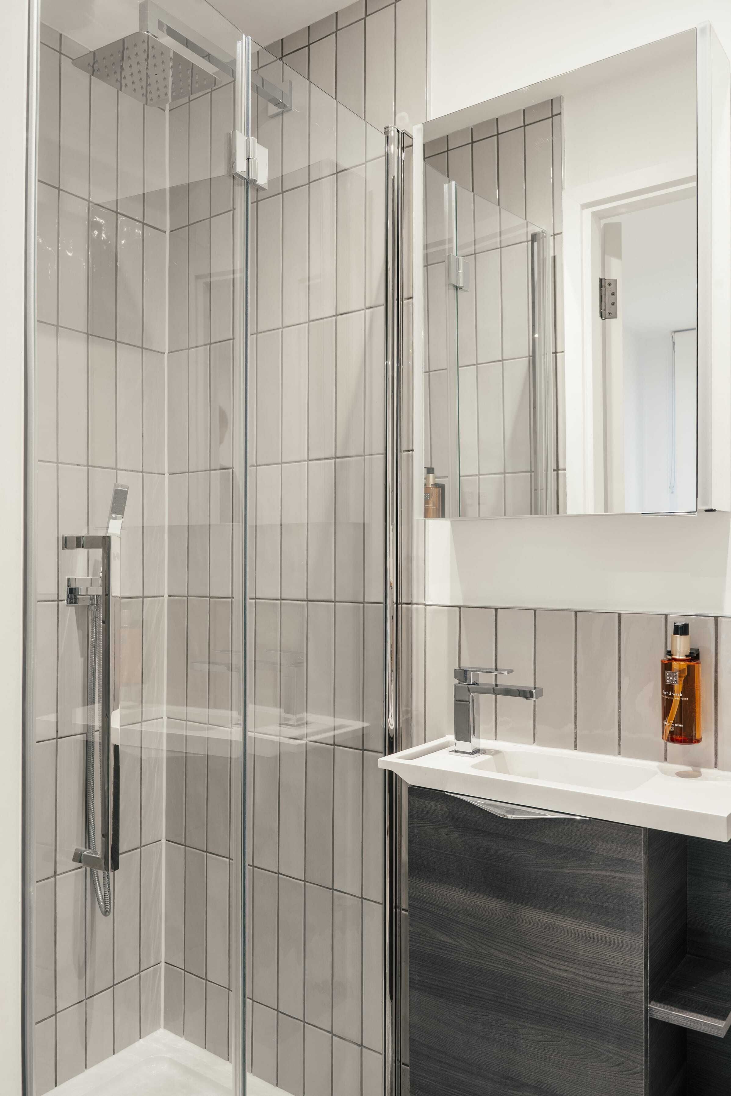 A modern bathroom with a glass-enclosed shower, a white sink, and a dark wood vanity.