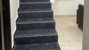 A staircase with dark marble steps leading upwards, a white wall on the right, and a wooden door on the left. - Kiana's Funstay (Lonavala)