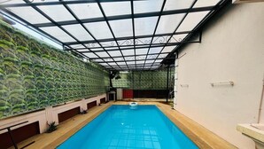 An indoor swimming pool with a clear ceiling and walls adorned with a green leafy pattern. - Kiana's Funstay (Lonavala)