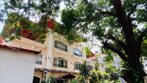 A two-story building with a balcony, surrounded by lush greenery and a large tree. - Kiana's Funstay (Lonavala)