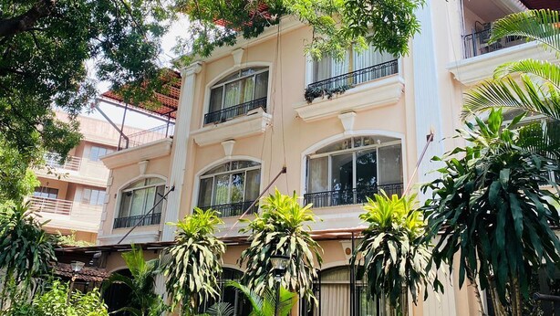 A multi-story building with balconies, surrounded by lush greenery and various plants. - Kiana's Funstay (Lonavala)