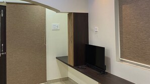 A modern hotel room with a wooden ceiling, a flat-screen TV on a wooden console, a door, and an air conditioning unit. - Kiana's Funstay (Lonavala)