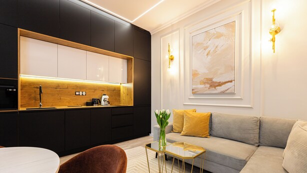 A modern living room with a sofa, a glass coffee table, and a kitchen area with dark cabinetry and a wooden countertop. - Native Apartments Kołłątaja 12 (Kraków)