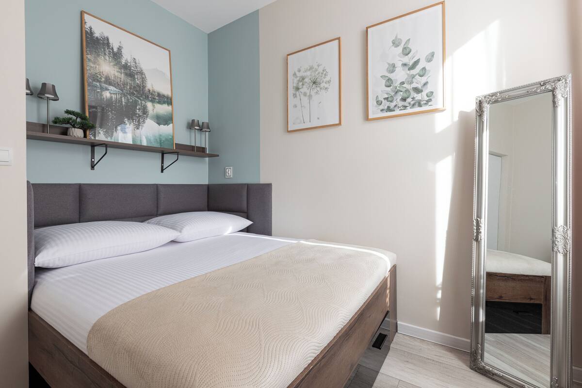A neatly made bed with a headboard, a bedside table, and a large mirror.